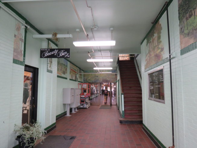 The 1 Public Square entrance to the Paddock Arcade features a series of murals highlighting historic Watertown, NY, and the entrance to the Beauty Bar, where the story goes a previous iteration did include special beverages as part of the salon experience. Photo by Camilla Ammirati, 2017.