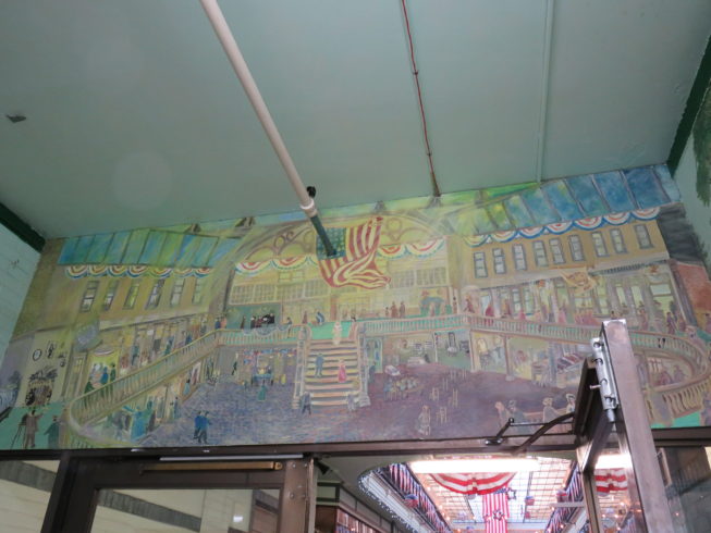 An entryway features a set of murals by local artist Ronald Collins, depicting themes from the Paddock Arcade’s 19th-century days as a place for the fashionable to see and be seen, to the Watertown origins of the Woolworth’s five-and-dime store chain, to the bustling Jefferson County Fair, celebrated locally as the oldest continually running fair in the country. Photo by 
Camilla Ammirati, 2017.